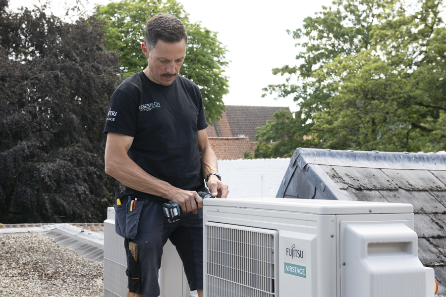 Fabrice staat op een dak in Eeklo om een lucht lucht warmtepomp na te kijken voor onderhoud van het merk Fujitsu