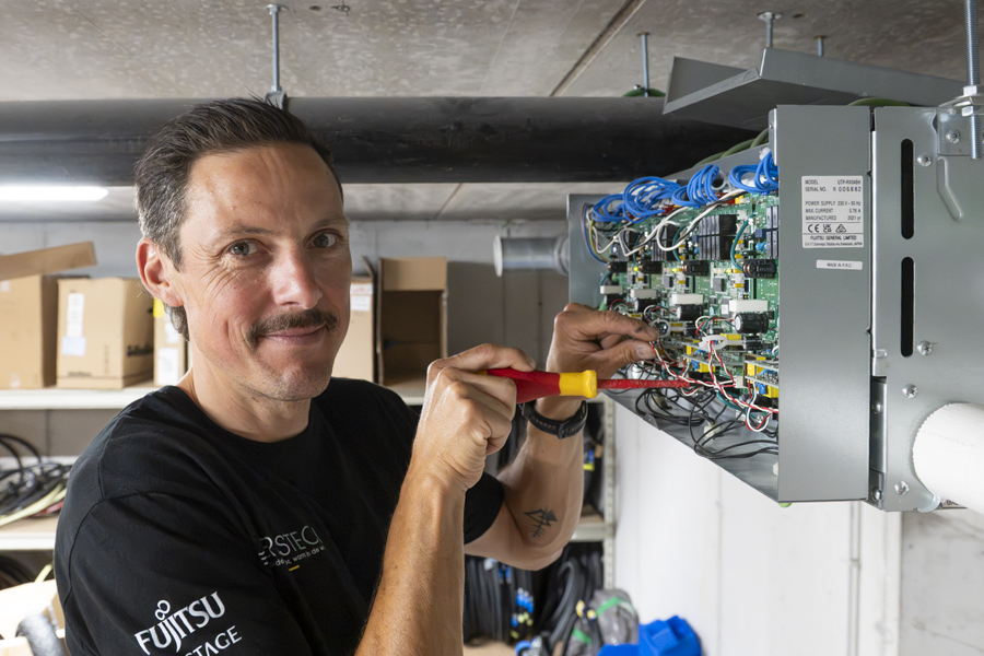 Fabrice glimlacht in de camera terwijl hij een airco systeem klaar maakt