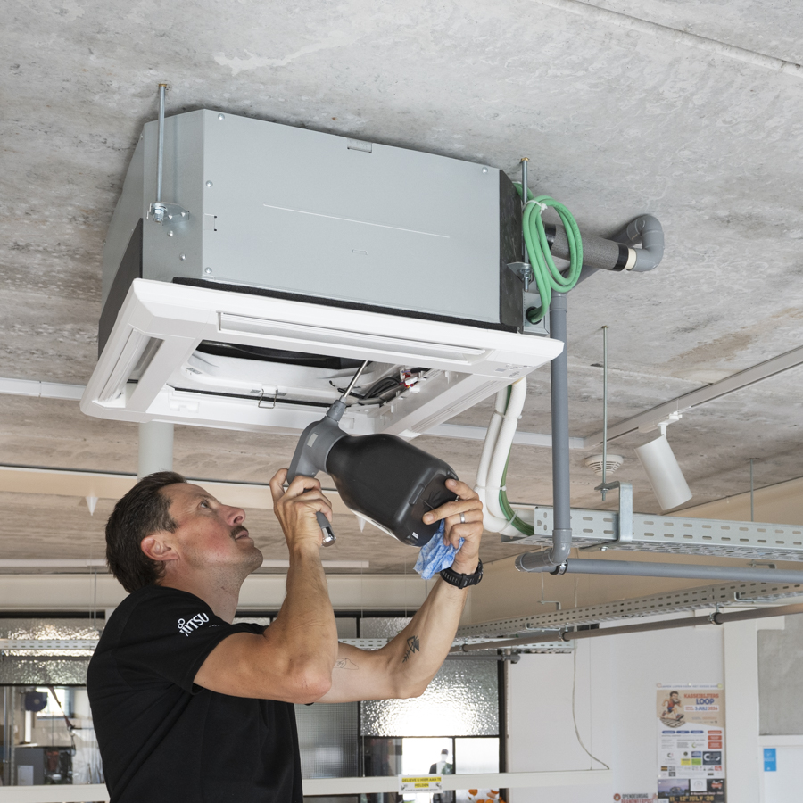 Fabrice spuit product in een airco unit bij een onderhoud in een handelspand.
